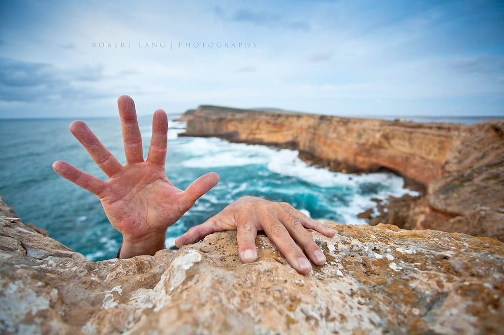 Image of a cliff on the ocean and hands reaching over the cliff