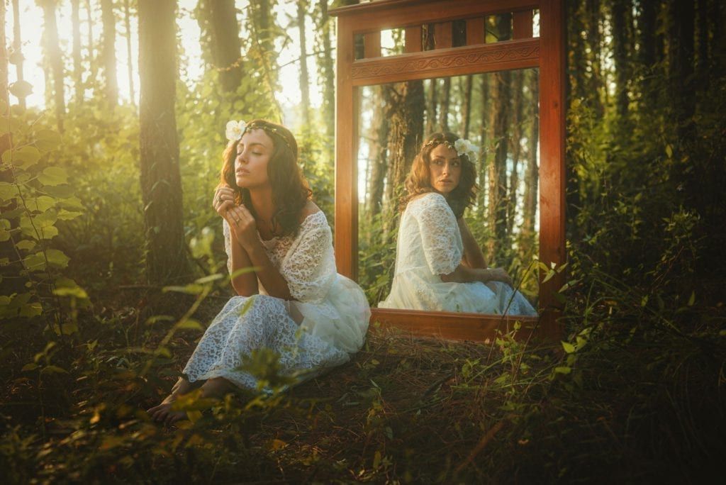 Image of a woman in the woods looking into a mirror